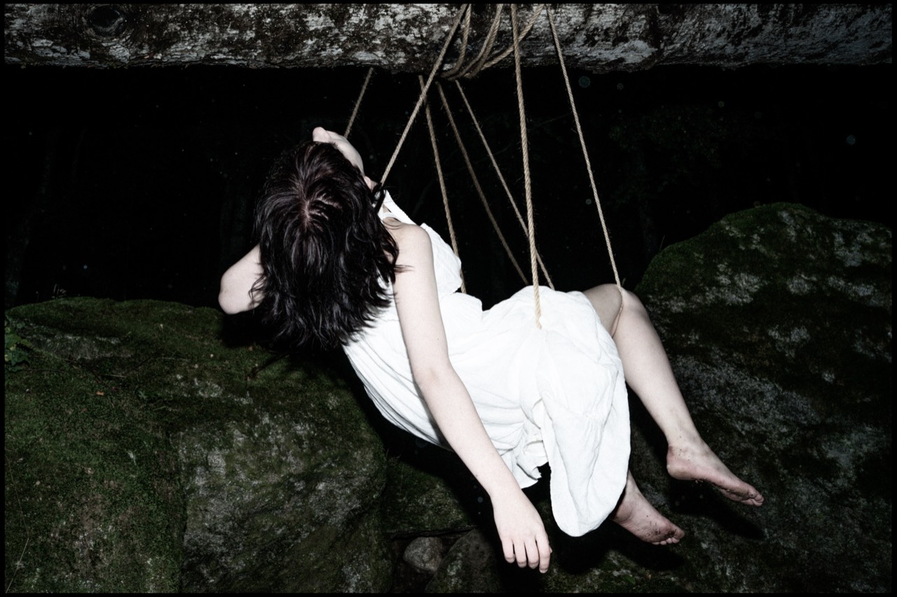 Tied — Anfisa reclining in a rope cradle against dark rock, Italian Alps; photograph by Tom Pradella