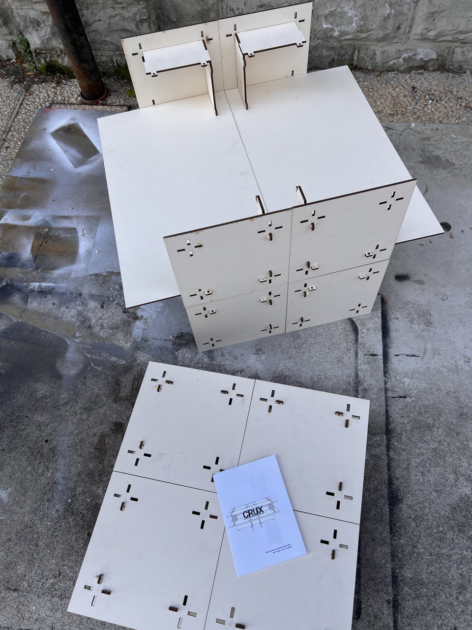 CRUX — laser-cut prototype parts and assembly booklet laid out on pavement